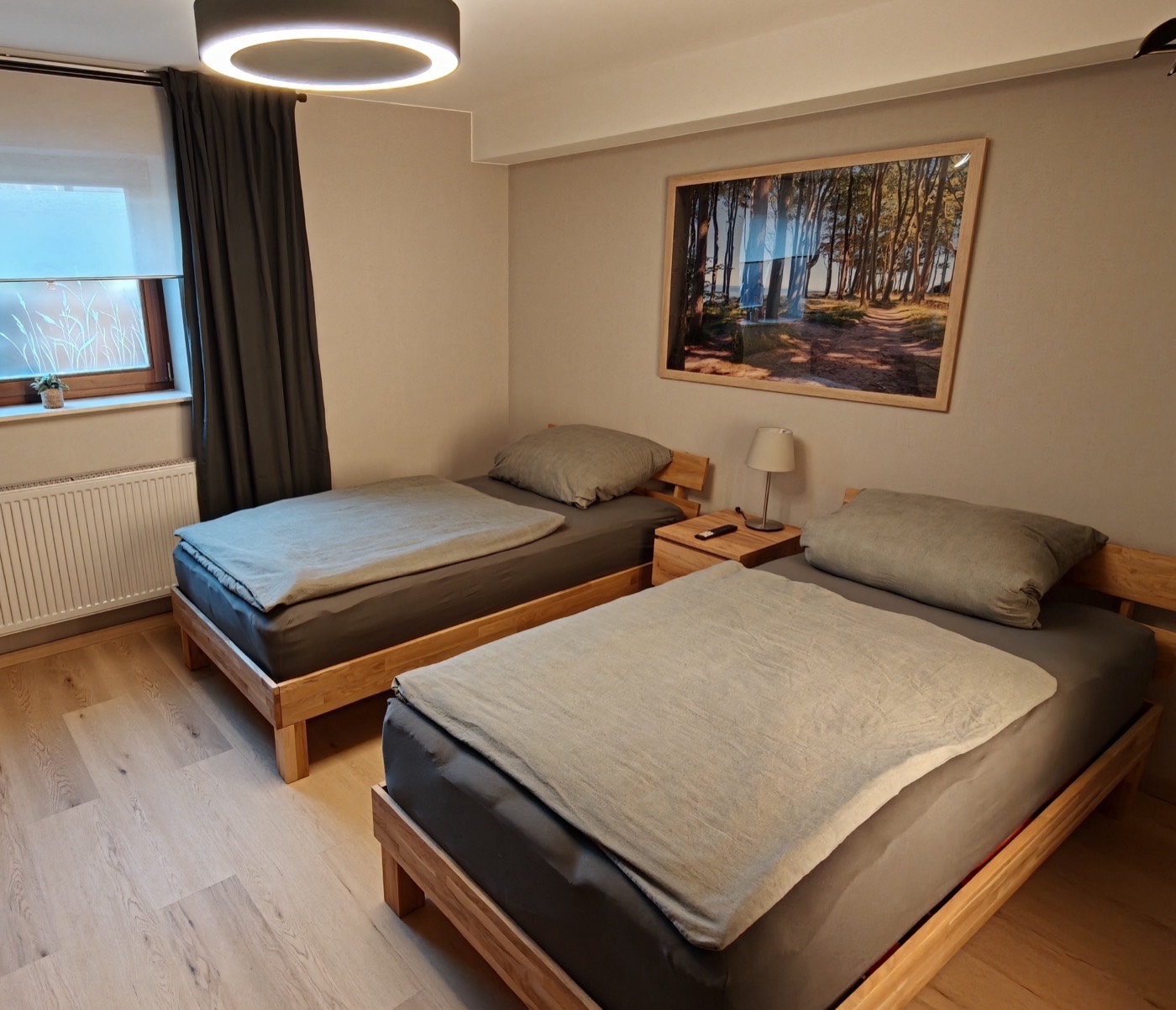 Frisch renoviertes Schlafzimmer mit zwei Massivholzbetten und beleuchteter Holz-Lamellenwand